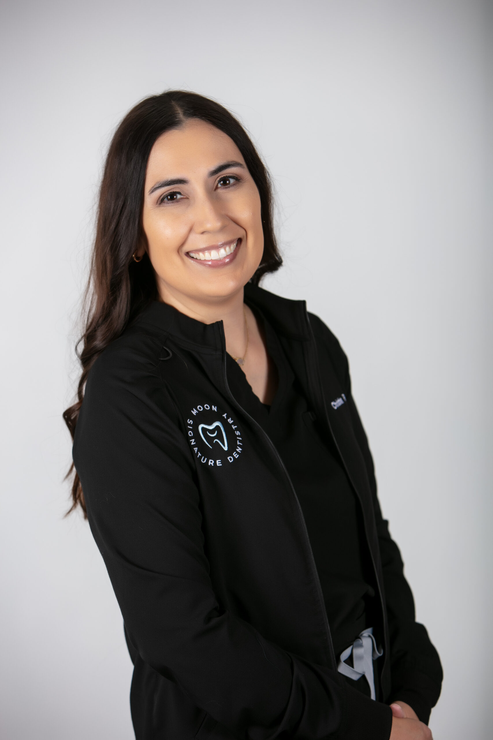 Dental hygienist Christina smiling in a black uniform with Moon Signature Dentistry logo, representing compassionate dental care in Olathe.