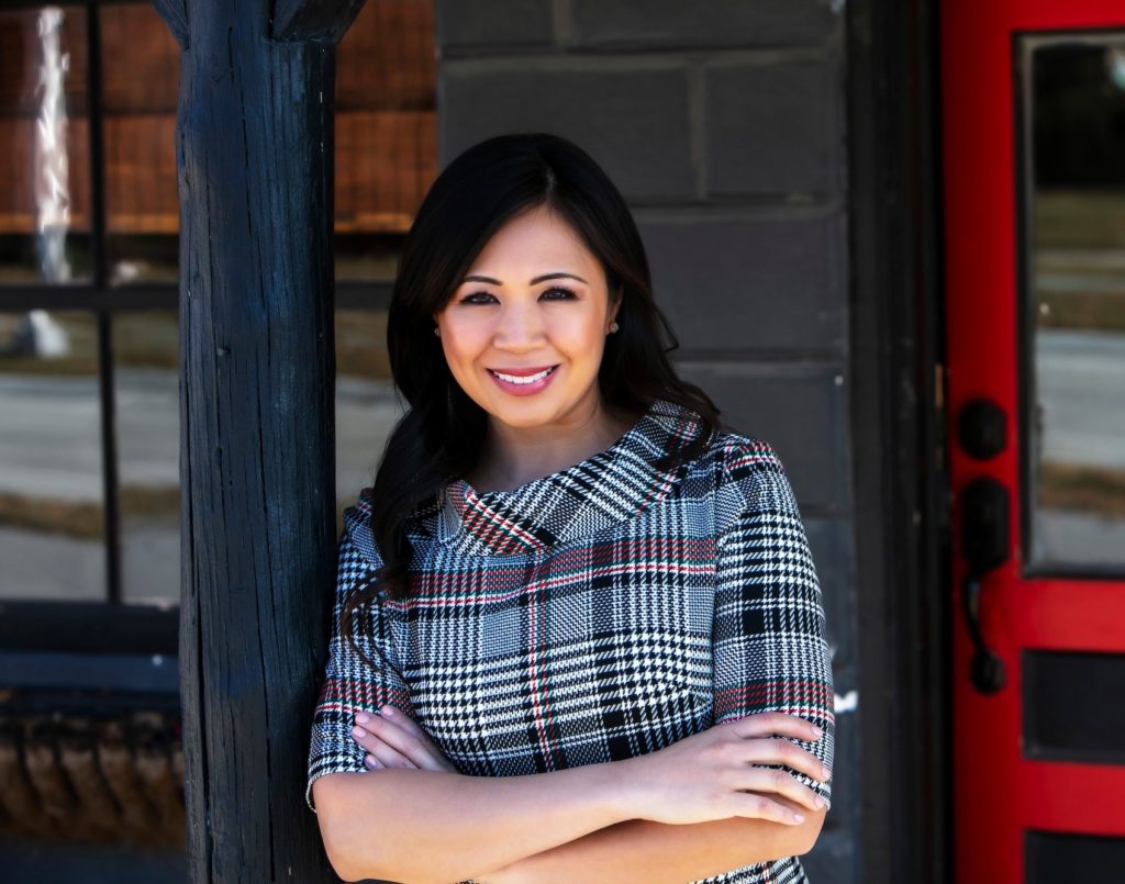 Dr. Beverly Moon, cosmetic dentist in Olathe, smiling confidently in a plaid coat, standing outside Moon Signature Dentistry.