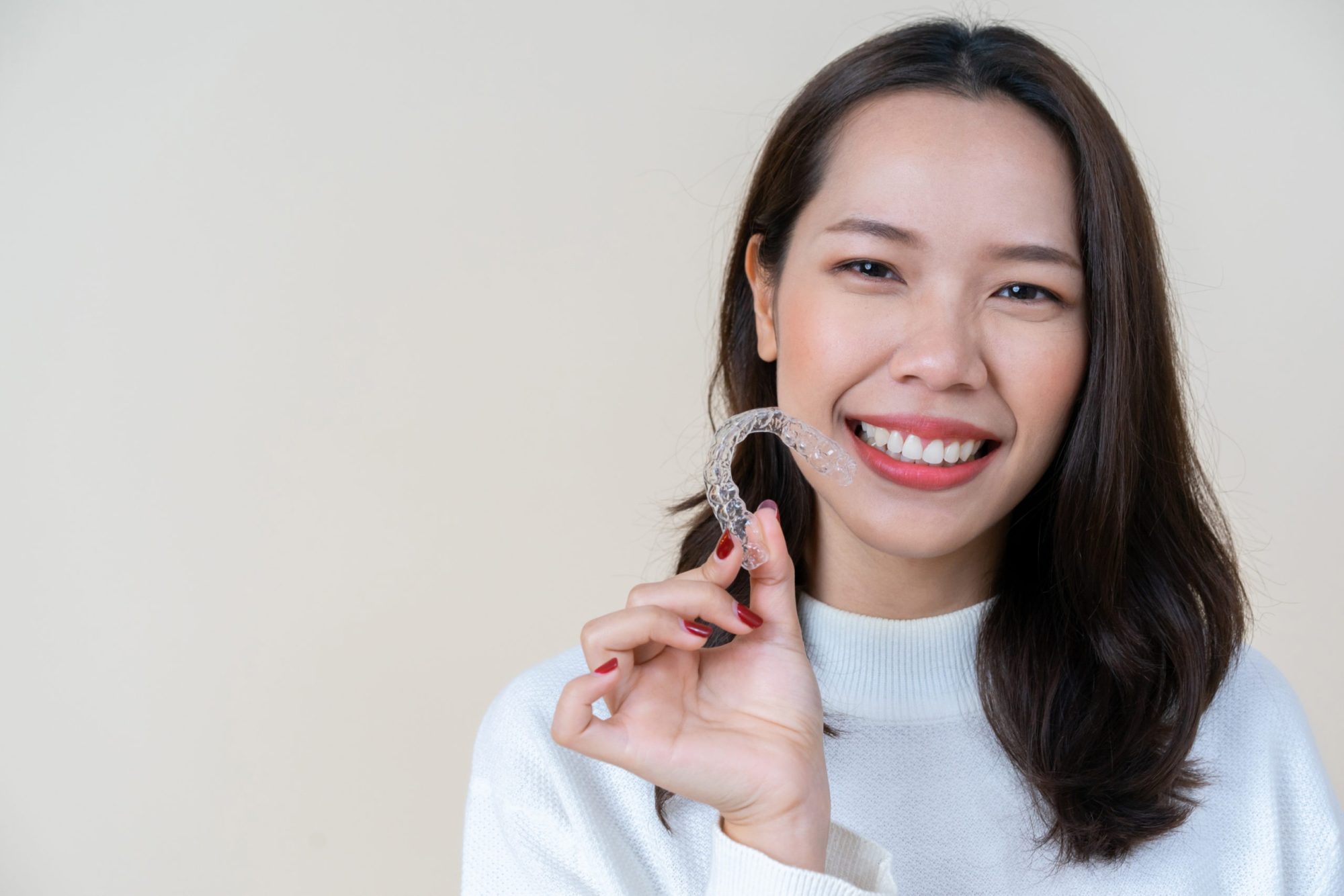 Woman smiling while holding Invisalign aligner, showcasing clear orthodontic treatment option at a cosmetic dentist in Olathe.