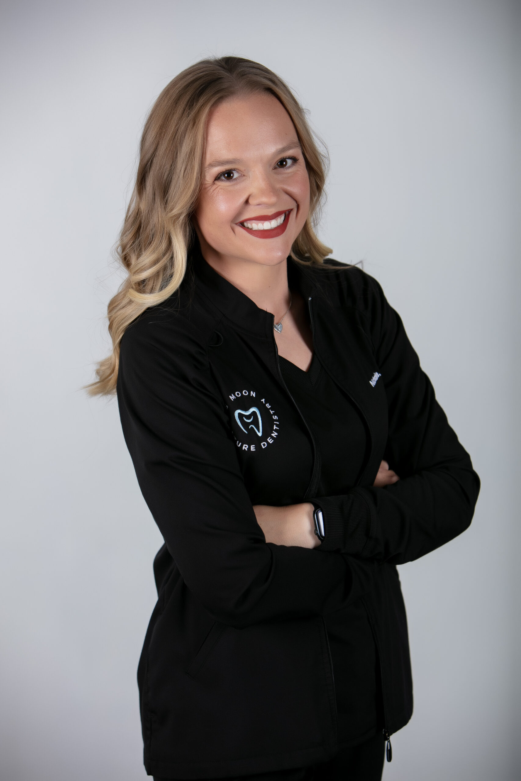 Dental hygienist Nichole smiling in a black jacket with Moon Signature Dentistry logo, representing compassionate care in Olathe restorative and cosmetic dentistry.